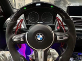 A BMW steering wheel with red paddle shifters is centered, displaying the logo and 