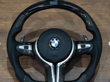 The object is a BMW car steering wheel with paddle shifters and control buttons, placed on a wooden surface. Text visible includes 
