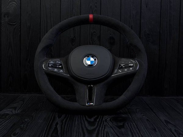 A black BMW steering wheel, showing control buttons on both sides and a central logo, is set against a dark wood-paneled background. Text includes: "BMW," "AIRBAG," and various button labels.