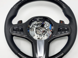 A carbon-fiber and leather car steering wheel, with integrated buttons and exposed wiring in the center, set against a plain white background.