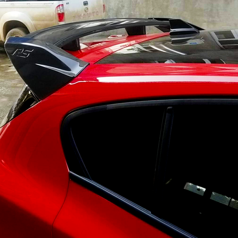 A red car features a black spoiler with "RS" embossed on it, parked in an outdoor setting beside another vehicle against a concrete wall.