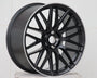 A matte black alloy wheel with a multi-spoke design is resting on a white, textured surface, set against a plain white background.