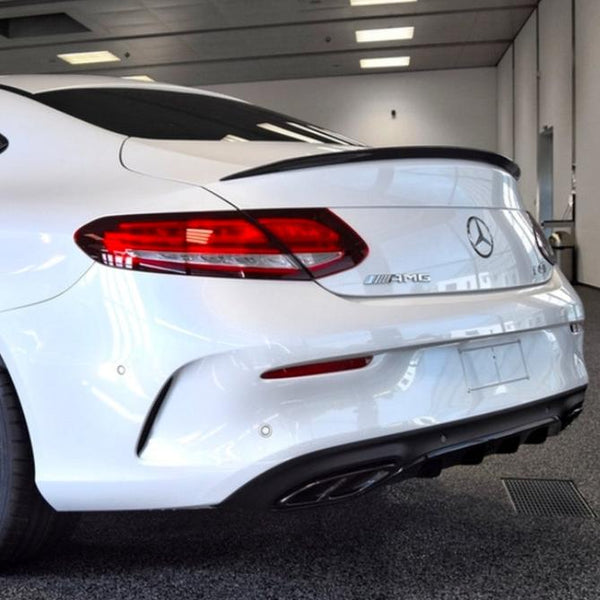 A white Mercedes-Benz AMG car is stationary in a well-lit indoor showroom. The emphasis is on its rear, featuring sleek taillights, a glossy finish, and dual exhausts.
