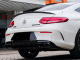 A white Mercedes-Benz C 300 AMG is parked on a cobblestone surface. The car's rear features dual exhausts and red tail lights, with an orange and white building in the background.