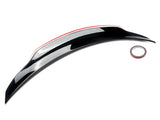 A glossy black car spoiler sits on a white background, accompanied by a small roll of adhesive tape, emphasizing its installation purpose.