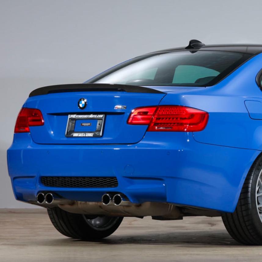 A blue BMW car is parked indoors, focused on its rear end with dual exhaust pipes. The license plate reads "www.forsale.com, BMW SALES SERVICE."