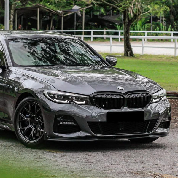 A sleek gray car, parked on a paved area, features distinctive front grille and sharp headlights, surrounded by lush green grass and trees.