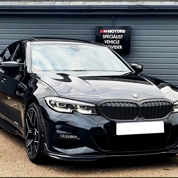 A black sedan, parked in front of a gray building, features sleek design elements. The sign reads "A6 Motors Specialist Vehicle Provider." The environment appears to be a dealership.