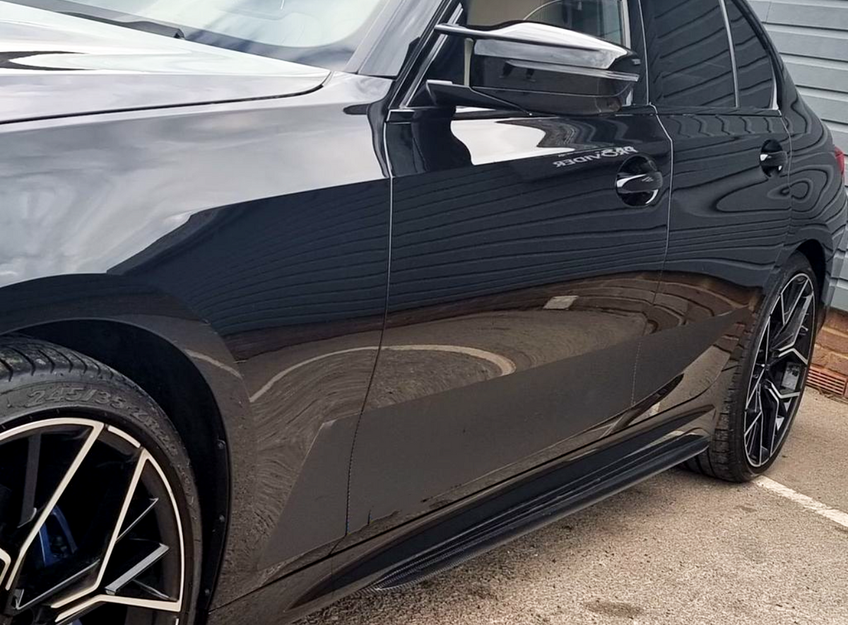 A polished black car with "BYONDXR" on the side door is parked on a concrete surface. Its sleek exterior reflects nearby structures, showcasing detailed angular rims and precise body lines.
