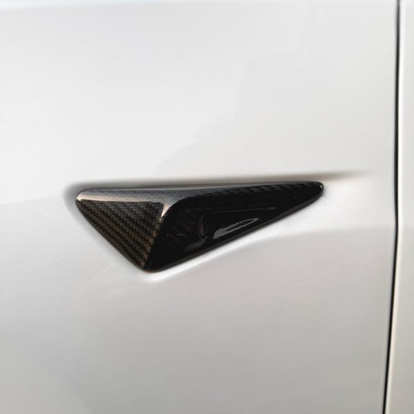 A triangular, carbon fiber car camera protrudes from a smooth, white vehicle surface, suggesting advanced technology integration for automotive safety and design enhancement.