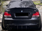 Car, stationary in a wet, winding road environment; it's black with tinted windows, dual exhausts, and a BMW logo. Surrounding context includes greenery and guardrails.