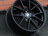 A BMW car rim, featuring a multi-spoke design and centered logo, leans against a textured brick wall on a rough concrete ground.