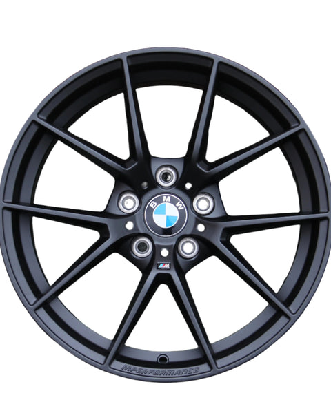 A black alloy wheel with a multi-spoke design features a BMW emblem in the center. The text "M PERFORMANCE" is written along the bottom, set against a white background.