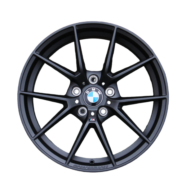 A black alloy wheel with a multi-spoke design features a BMW emblem in the center. The text "M PERFORMANCE" is written along the bottom, set against a white background.