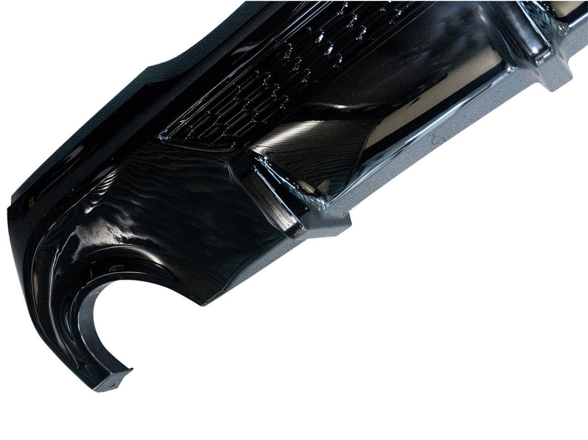 A glossy black car bumper with an intricate design is displayed against a plain white background, showcasing its sleek curvature and surface details.