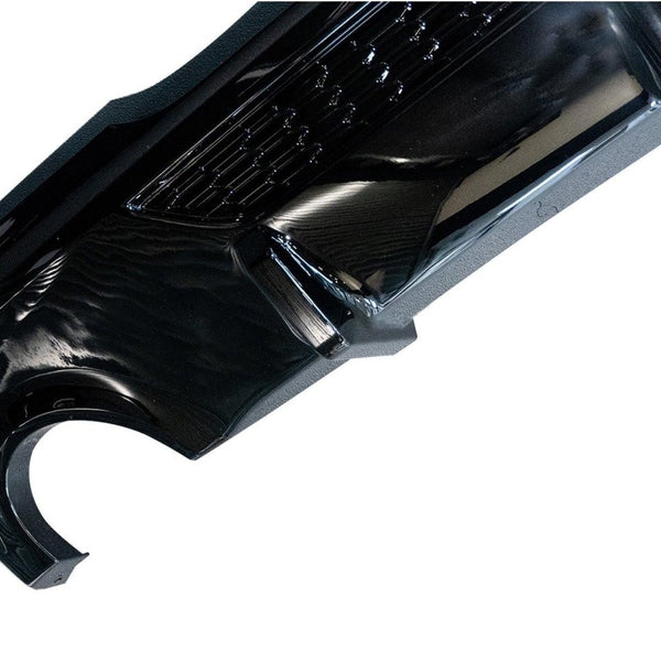 A glossy black car bumper with an intricate design is displayed against a plain white background, showcasing its sleek curvature and surface details.