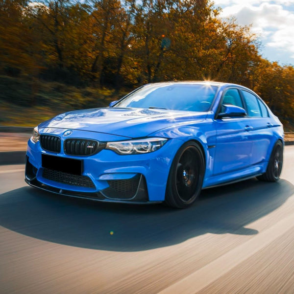 A blue car drives quickly down a road, surrounded by autumn trees with golden leaves under a cloudy sky.