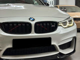 A white BMW car with illuminated headlights is parked indoors; the front grille features the BMW logo and 