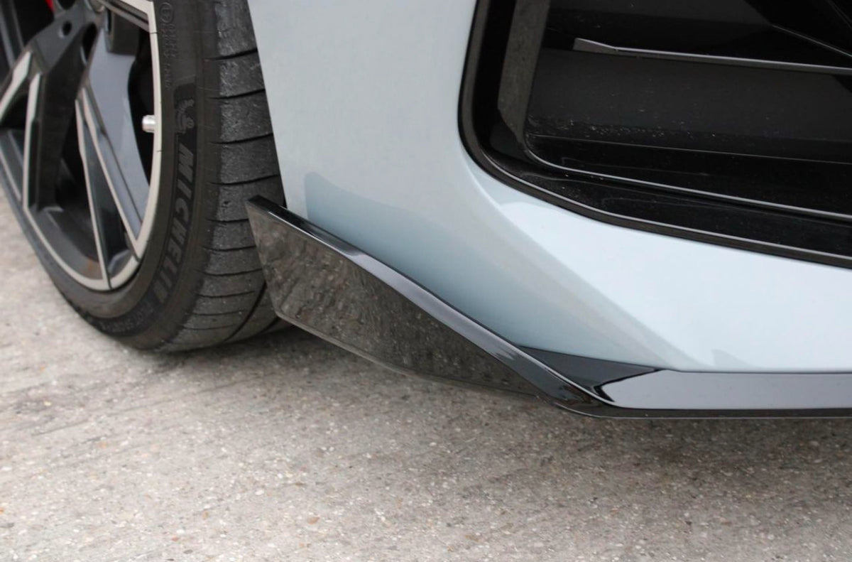 A car tire displays the "MICHELIN" logo, resting on concrete, adjacent to a glossy black aerodynamic trim on the rear bumper, suggesting a sporty vehicle design in a static setting.