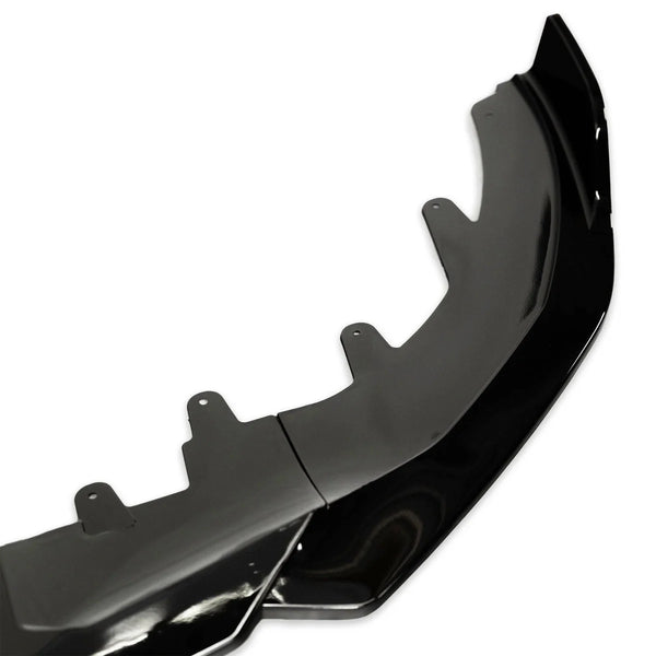 A black car front splitter, featuring multiple mounting tabs, is shown in close-up on a white background, highlighting its glossy finish and aerodynamic design.