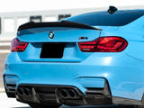 A blue BMW M4 car is parked in a sunlit area, showing its rear view with four exhaust pipes and a black spoiler. The BMW logo is visible, and the setting is urban.