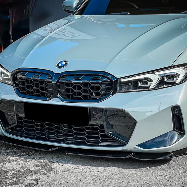 A white BMW car is parked, featuring a distinctive front grille and sleek headlights. It is situated on a paved surface with a darker vehicle partially visible in the background.
