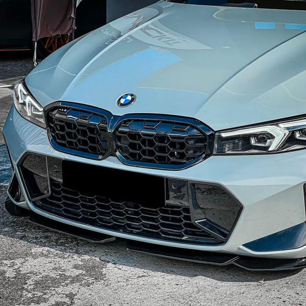 A light blue BMW car front is parked on a concrete surface. It features a prominent grille with a distinctive honeycomb design and angular headlights.