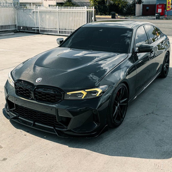 A sleek, dark gray BMW sedan is parked on a concrete surface, surrounded by a white fence and urban background, under clear daylight.