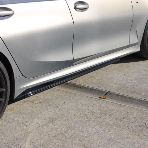 A silver car stands parked on a concrete surface. The focus is on the side, showing the door, handle, and a portion of the wheel, with a small drain visible below.