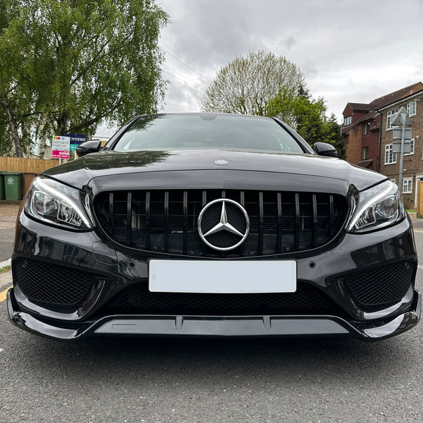 Black Mercedes car parked on a residential street with trees, brick buildings, and several trash bins in the background. A "For Sale" sign is visible among the greenery.