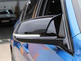 A black side mirror is attached to a blue car, reflecting light. The car is parked in a garage with another vehicle visible in the blurred background.