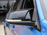 Car side mirror with a sleek black finish reflects its surroundings. It's attached to a blue vehicle parked in a garage, with another car barely visible in the background.