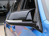 A sleek black side mirror is attached to a blue vehicle, reflecting its surroundings. The car is parked in an indoor area with concrete flooring and other vehicles visible in the background.