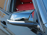 A sleek black car mirror reflects the blue sky and clouds, attached to a vehicle with red interior seats, parked near a brick wall.