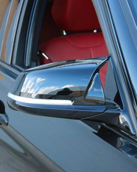 A sleek black car mirror reflects the blue sky and clouds, attached to a vehicle with red interior seats, parked near a brick wall.