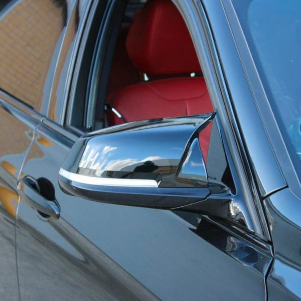 A sleek car side mirror reflects cloudy skies, attached to a black vehicle. The car's window is open, revealing a vivid red interior. The background shows a brick wall.