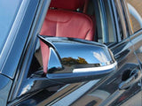 A black car's side mirror reflects outdoor scenery, with trees and sky. The car interior features a red leather seat visible through the open window.