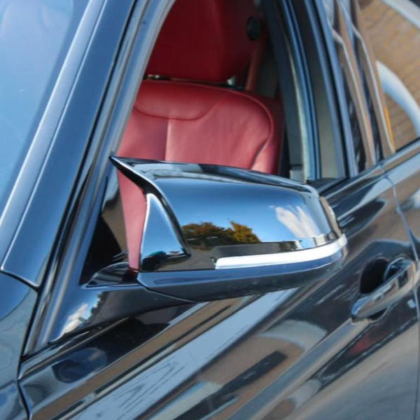 A black car's side mirror reflects outdoor scenery, with trees and sky. The car interior features a red leather seat visible through the open window.
