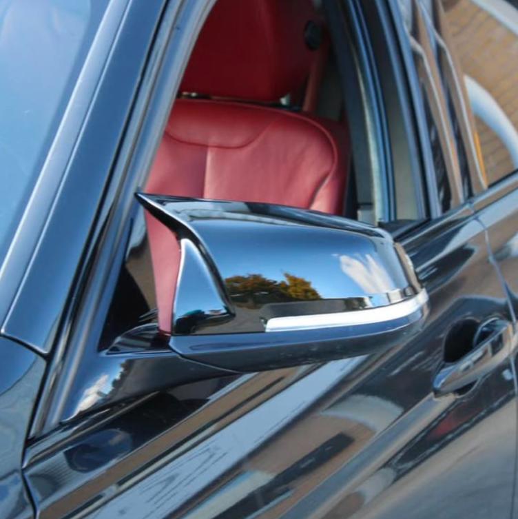 A black car's side mirror reflects outdoor scenery, with trees and sky. The car interior features a red leather seat visible through the open window.