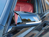 A black car door's side mirror reflects the sky and trees, positioned outside a vehicle with visible red leather interior. The context suggests an urban or suburban environment.