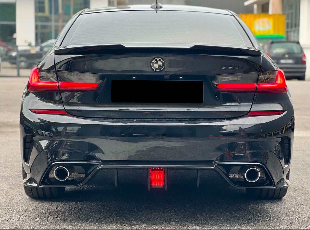 A black BMW 530i is parked, showing its rear view with illuminated taillights and dual exhausts. It's situated on a paved area near buildings.