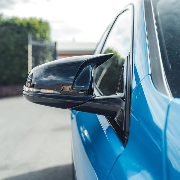 Side mirror reflecting sky, attached to a blue car. The background shows a blurred fence and greenery under partly cloudy skies.