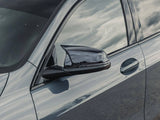 Car side mirror reflects sky and clouds, mounted on a sleek blue vehicle in an outdoor setting. The car door and handle are visible, highlighting modern automotive design.