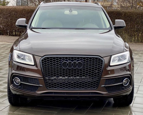 A brown Audi SUV parked on a tiled driveway, surrounded by leafless trees and residential buildings in the background, facing the camera directly.