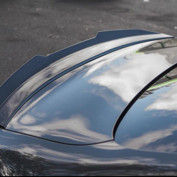 A shiny car roof reflects white clouds and blue sky, parked on a dark asphalt surface. The smooth surface emphasizes the car's sleek design.