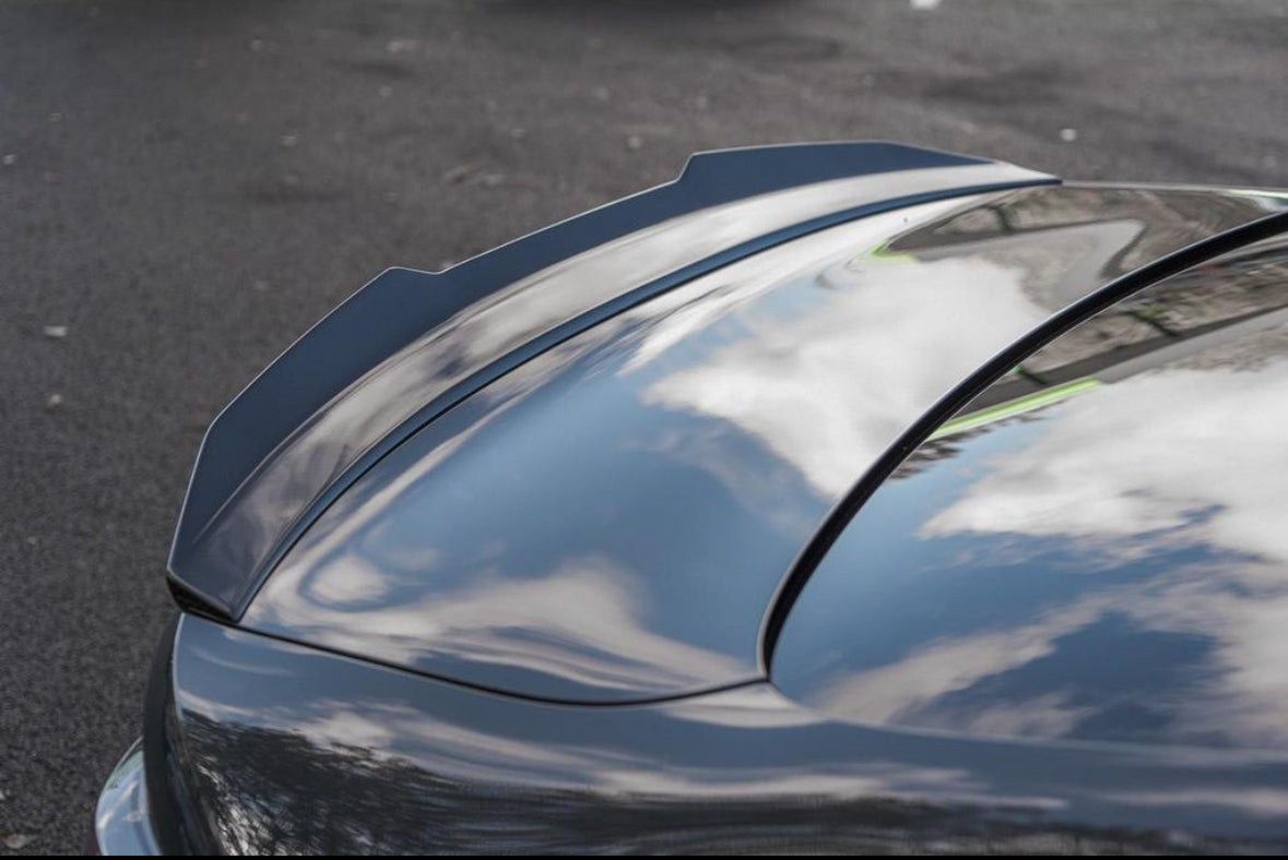 A shiny car roof reflects white clouds and blue sky, parked on a dark asphalt surface. The smooth surface emphasizes the car's sleek design.