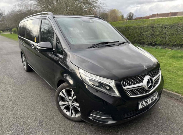 A black Mercedes van is parked on a suburban street. The road is bordered by hedges and trees. License plate reads "RO67 MYC".