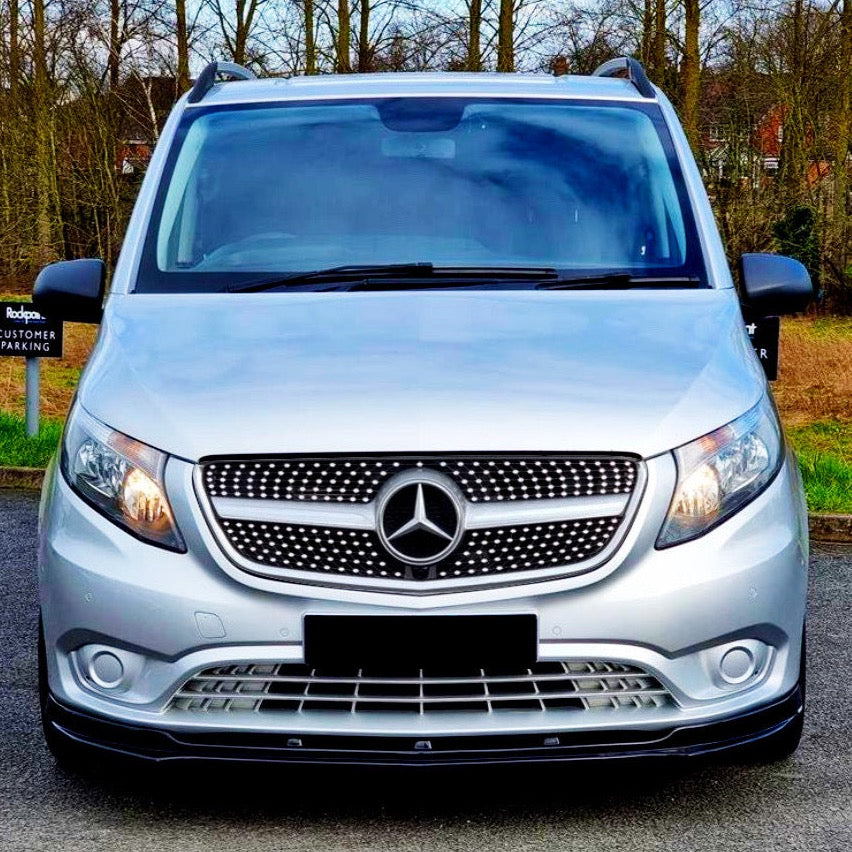 A silver van with a prominent Mercedes logo is parked on a road, surrounded by leafless trees and a grassy area. Signs read "Rodger's Customer Parking."
