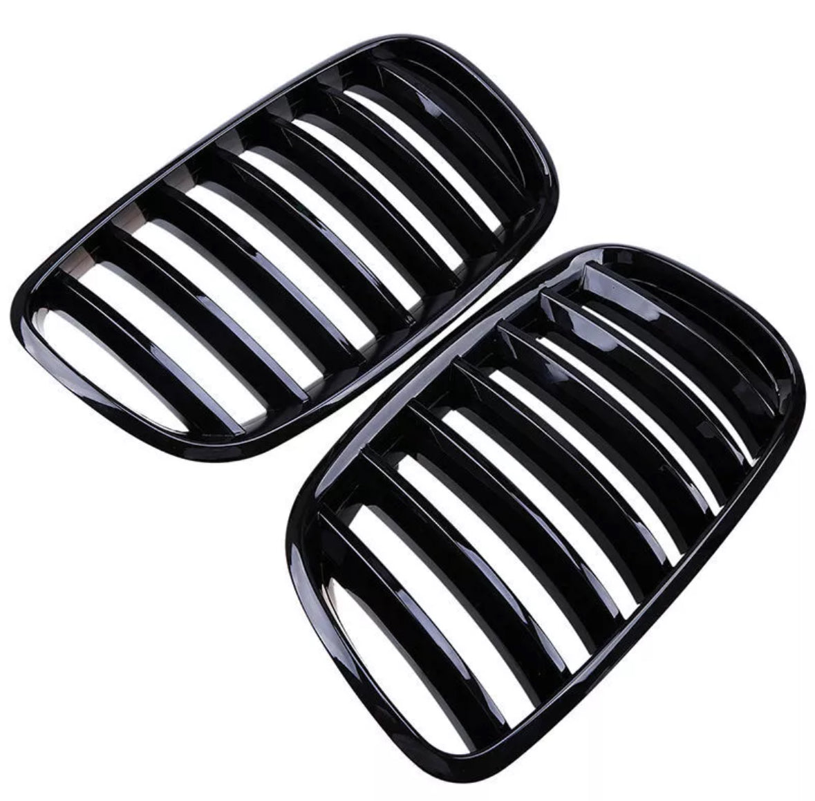 Black kidney-shaped car grilles with multiple vertical slats are placed side by side against a white background, showcasing their sleek, glossy finish.