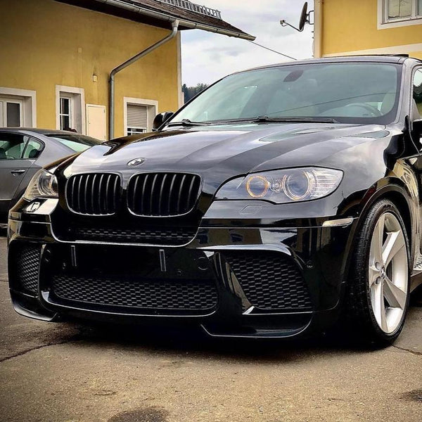 A black car parked in front of a yellow building, featuring prominent front grilles and alloy wheels, with another vehicle partially visible in the background.